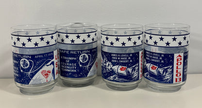 Four clear glass tumblers with blue and white space-themed designs celebrating the Apollo 11 moon landing, displayed side-by-side against a plain light background.