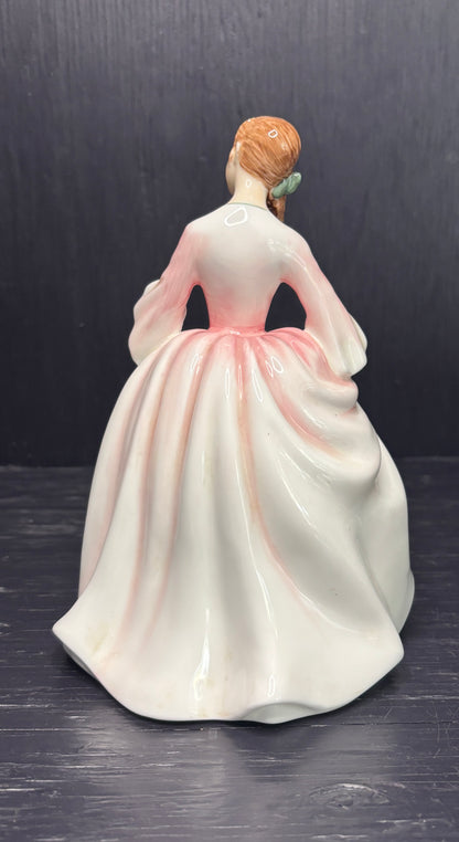 Porcelain figurine of a woman in a white dress with pink accents on a dark background