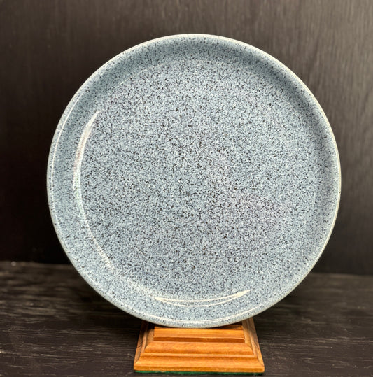 Speckled blue ceramic plate on a wooden stand against a dark background