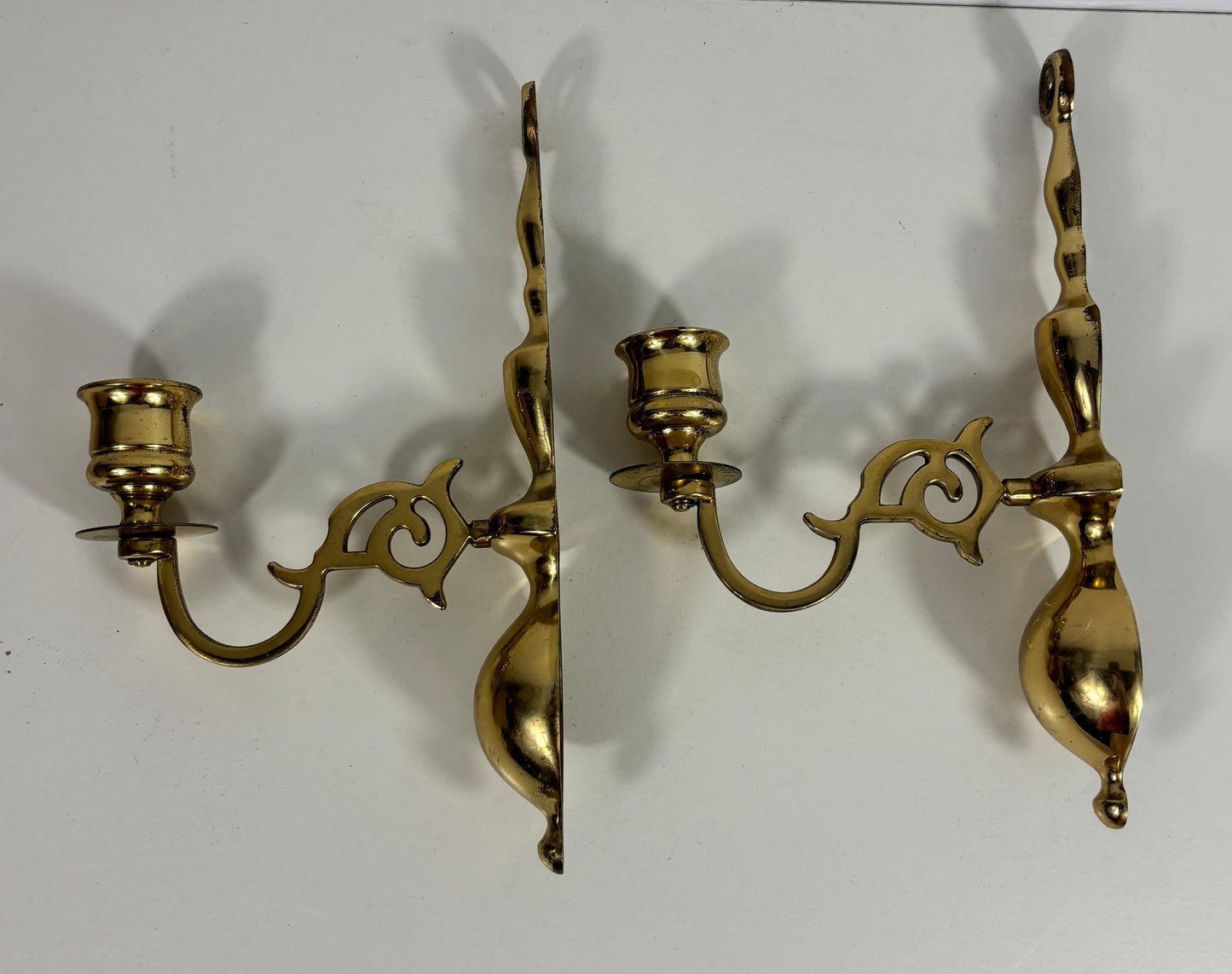 A pair of ornate brass wall sconces with curved arms and candle-style holders, shown against a plain white background.