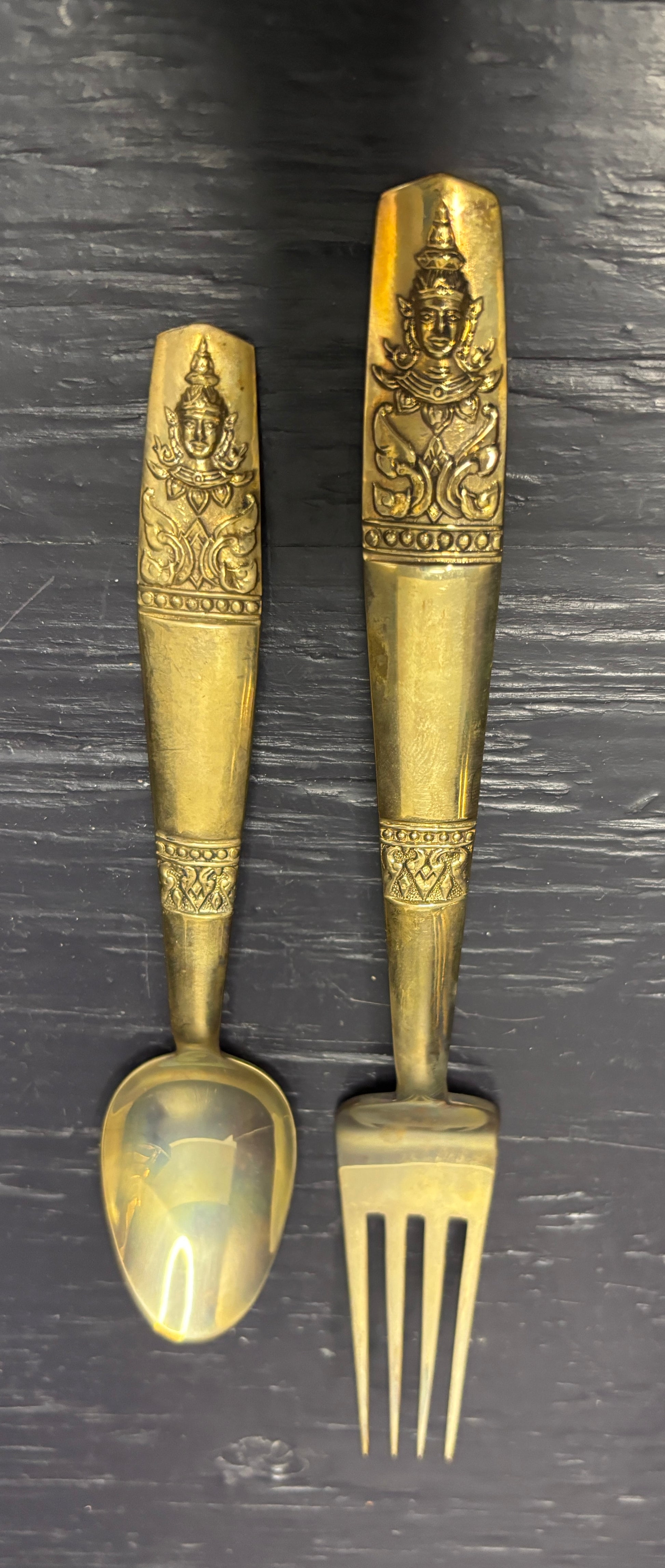 Pair of ornate brass spoon and fork on a dark surface