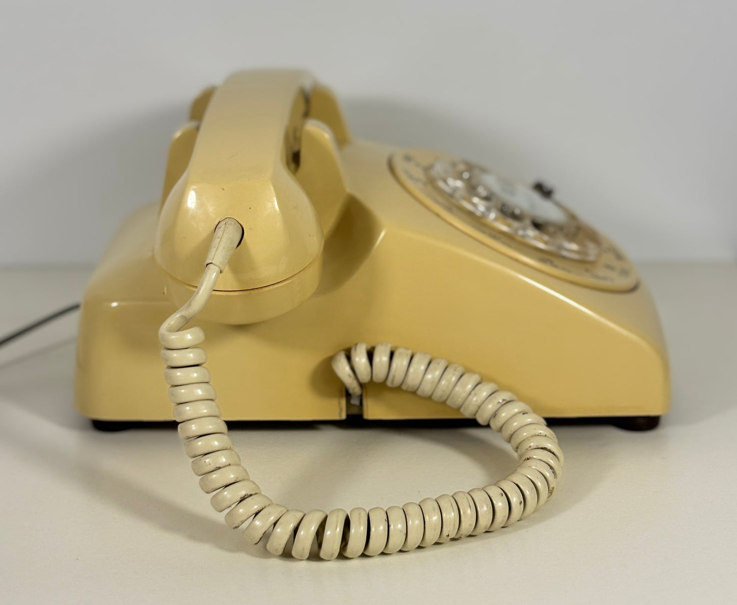 Beige rotary phone with coiled cord on a white background