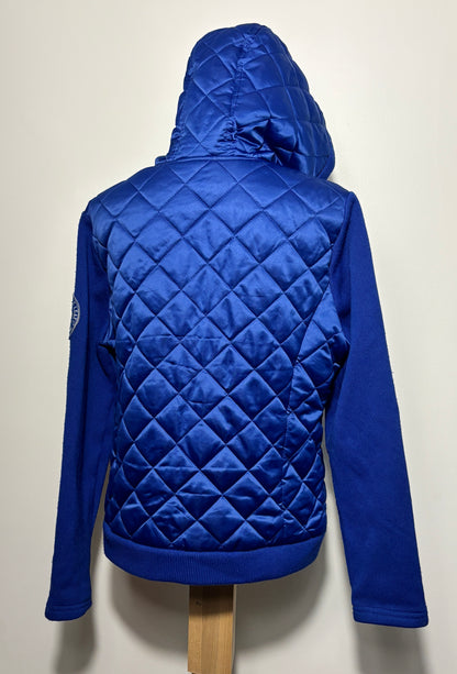 A royal blue quilted hooded jacket displayed on a wooden mannequin stand against a plain off-white wall, showing the back view with diamond quilting and solid blue sleeves.