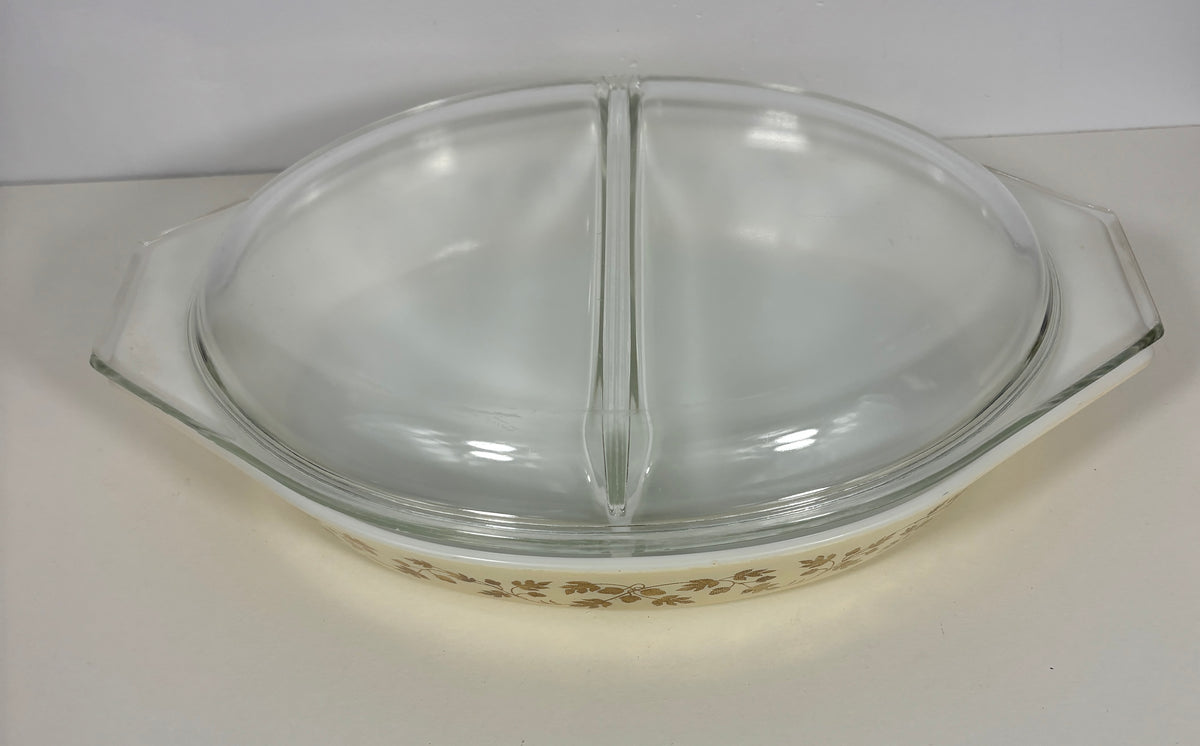 A vintage Pyrex glass divided baking dish with a clear glass lid, featuring a cream-colored base with a brown floral pattern.