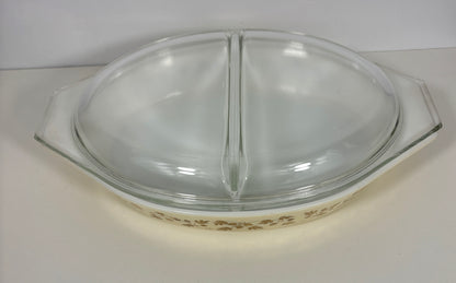 A vintage Pyrex glass divided baking dish with a clear glass lid, featuring a cream-colored base with a brown floral pattern.