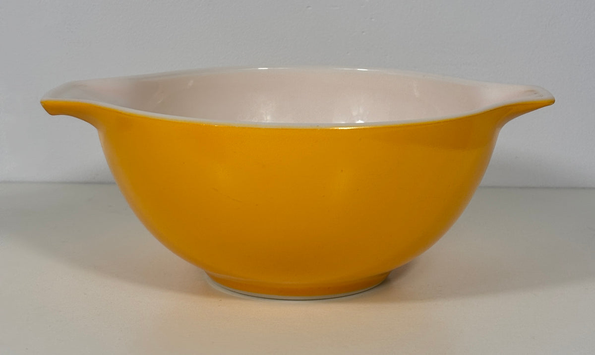A vintage yellow mixing bowl with a pale pink interior and small side handles, shown against a neutral light gray background.