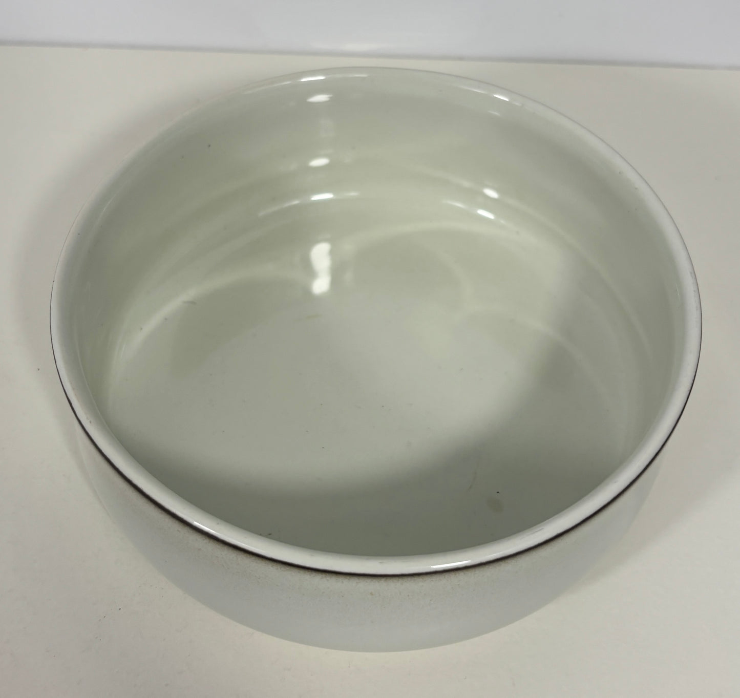 A white ceramic bowl with a thin dark rim, photographed from a top-down angle on a light surface.