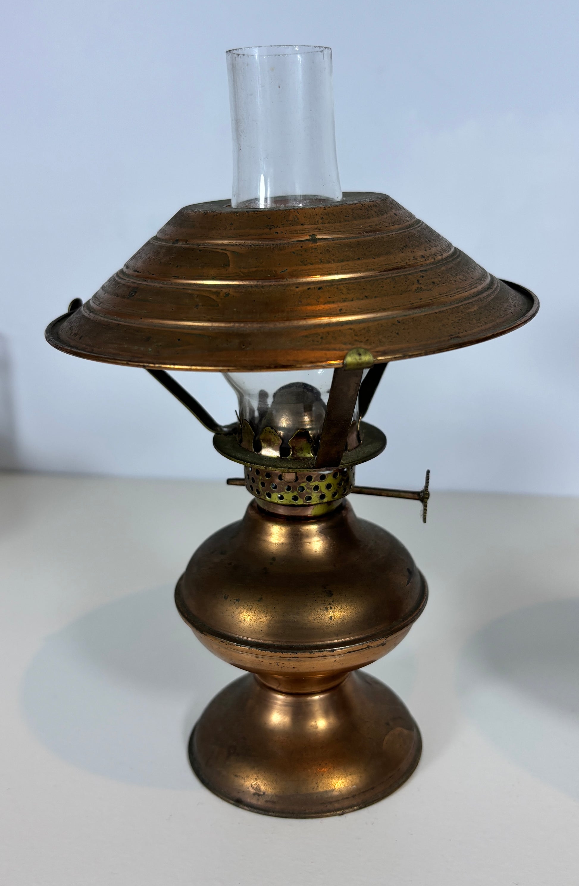 An antique brass oil lamp with a clear glass chimney, set against a plain light background.