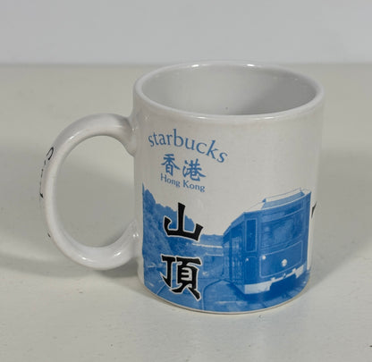 A white ceramic Starbucks mug with blue and black printed graphics, featuring the text 'starbucks Hong Kong' and Chinese characters, alongside a blue illustration of a tram.