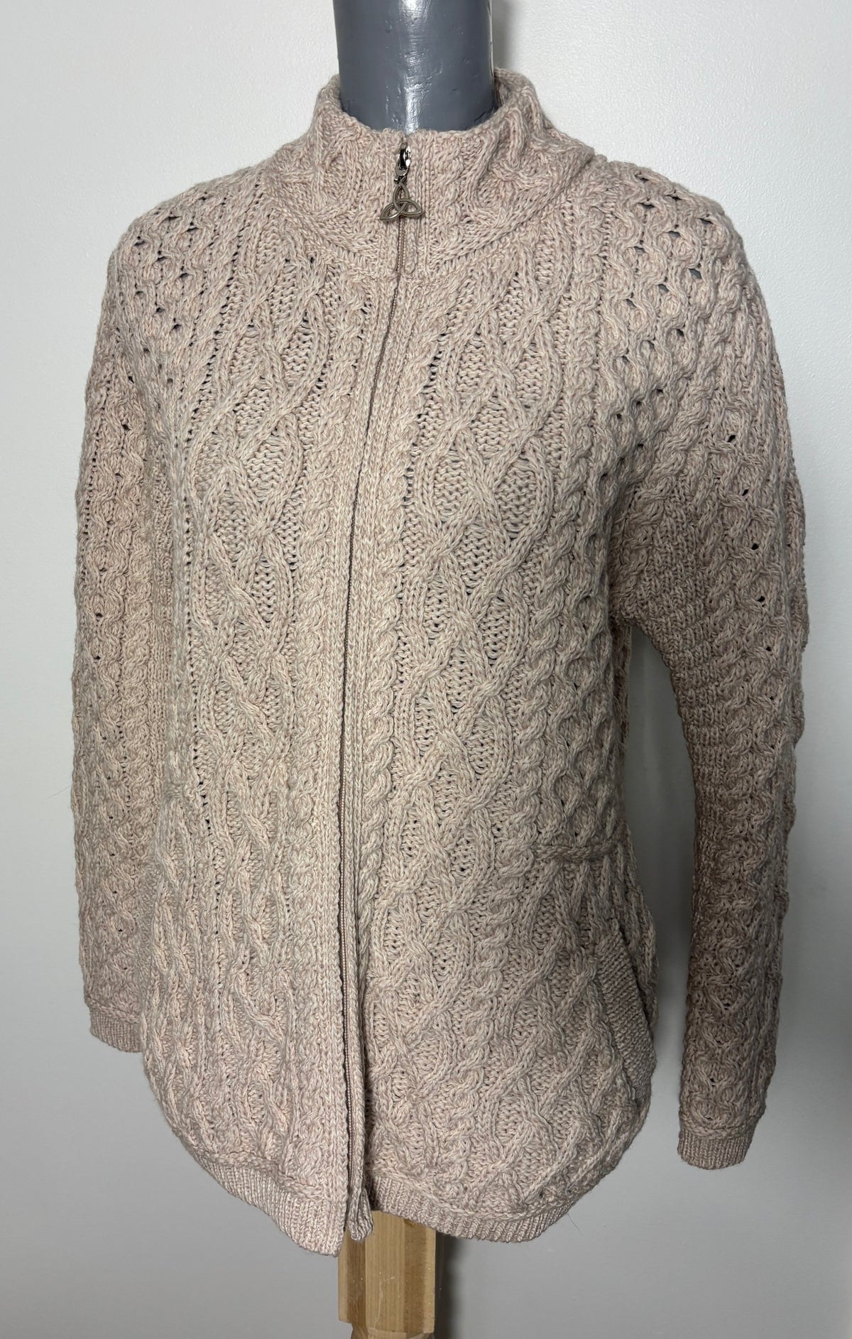 A cable-knit zip-up cardigan sweater in a light taupe-beige color, displayed on a gray mannequin torso against a plain light gray background.