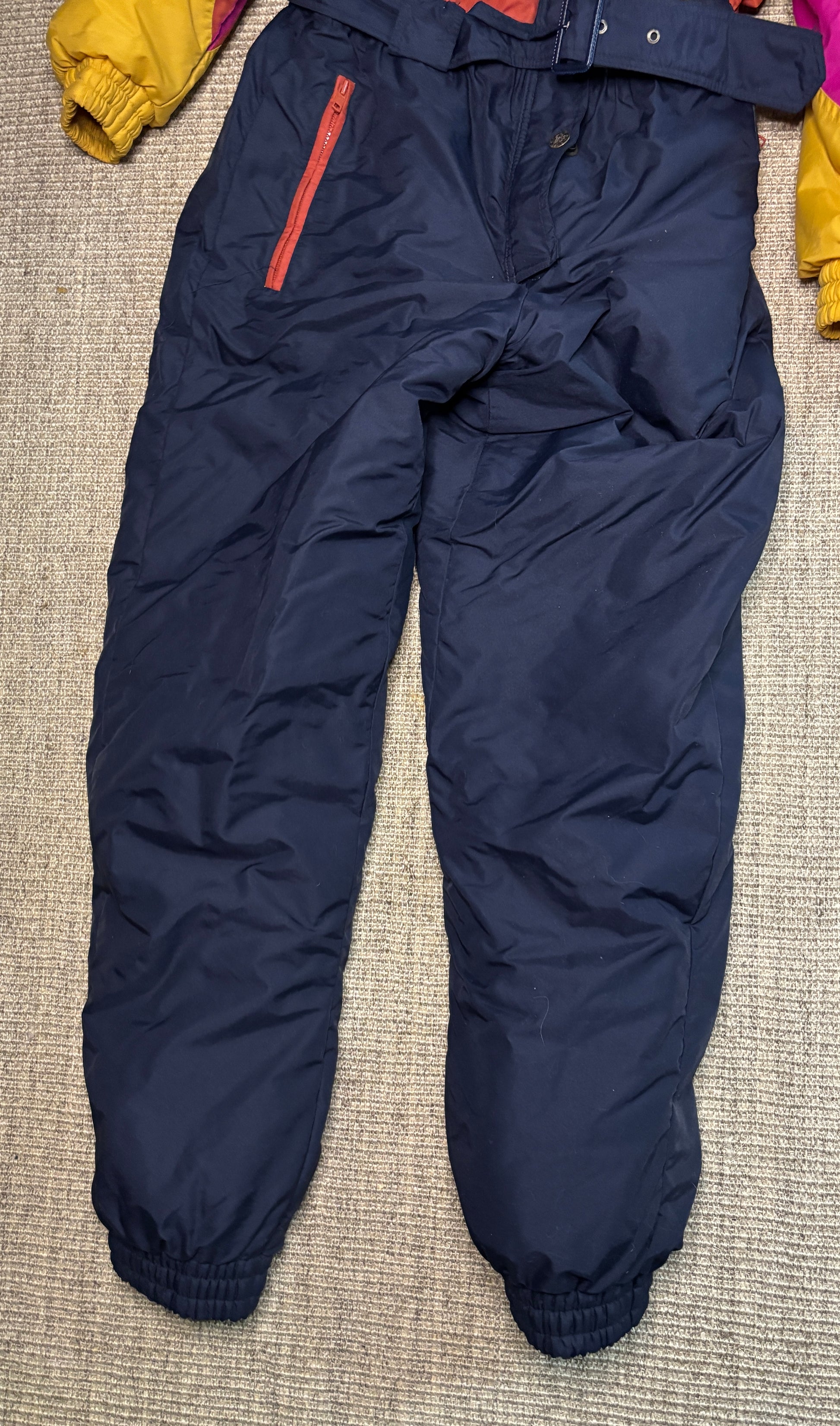 Navy blue snow pants with a red stripe on a textured surface