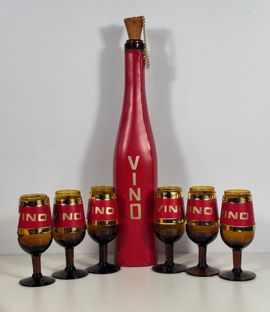 A vintage-style red wine bottle centerpiece with six matching amber and red wine glasses arranged in front on a white surface against a light gray background.