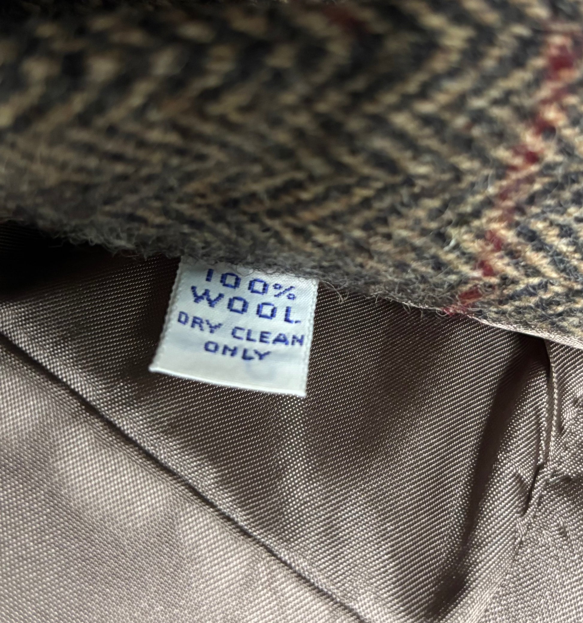 Close-up of a herringbone-patterned fabric with a '100% Wool Dry Clean Only' label.