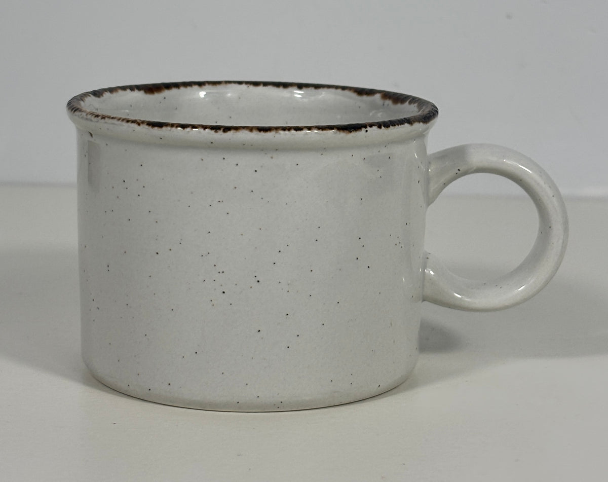 A speckled white ceramic mug with a dark brown rim and a loop handle, shown on a plain light background.