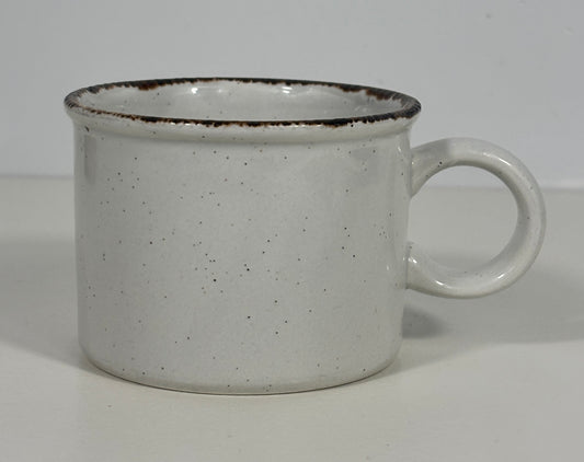 A speckled white ceramic mug with a dark brown rim and a loop handle, shown on a plain light background.