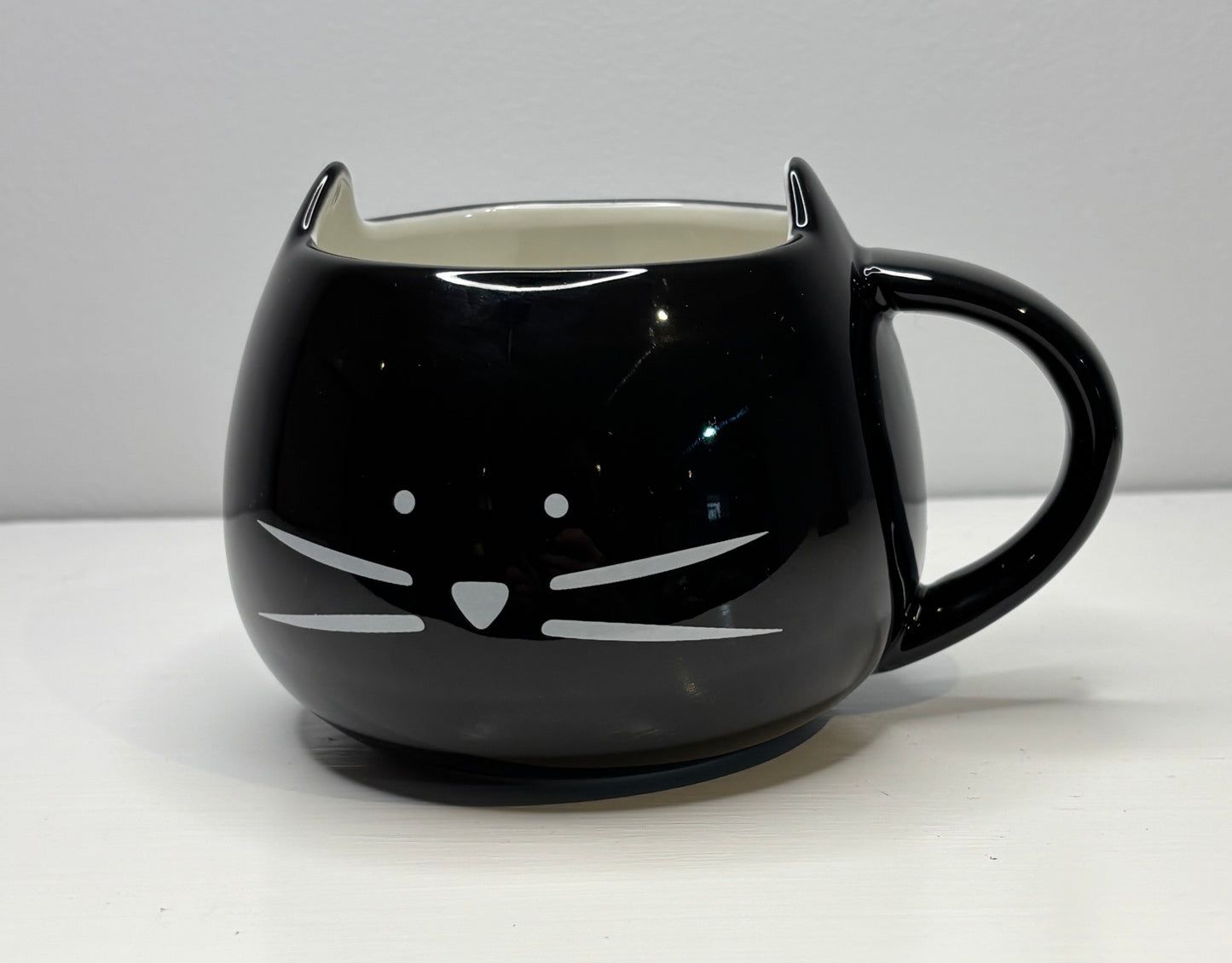 Black cat-shaped mug on a white surface with a gray background