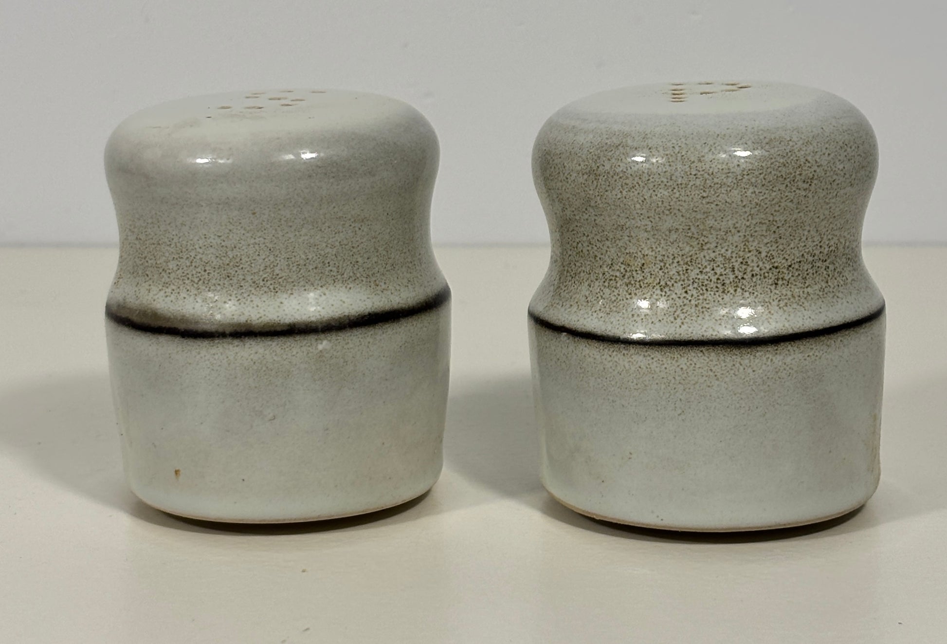 A pair of vintage ceramic salt and pepper shakers with a speckled gray and white glaze and a dark horizontal crack line, set against a plain off-white background.