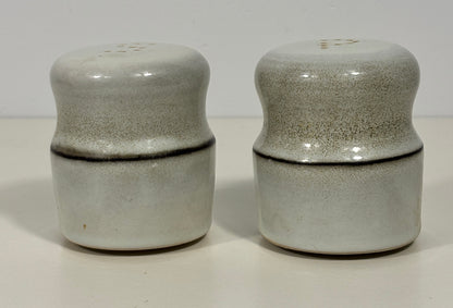 A pair of vintage ceramic salt and pepper shakers with a speckled gray and white glaze and a dark horizontal crack line, set against a plain off-white background.