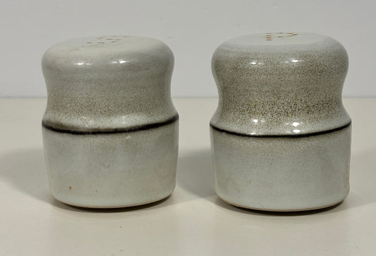 A pair of vintage ceramic salt and pepper shakers with a speckled gray and white glaze and a dark horizontal crack line, set against a plain off-white background.