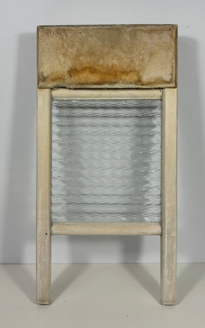 A vintage wooden washboard with a textured, ribbed glass or plastic panel and a weathered, stained top plate, set against a plain light gray background.