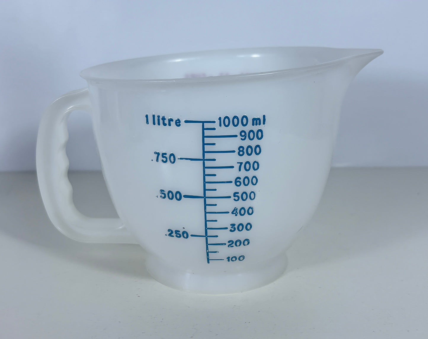 A translucent white plastic measuring jug with blue printed measurement markings in litres and millilitres, set against a plain light background.