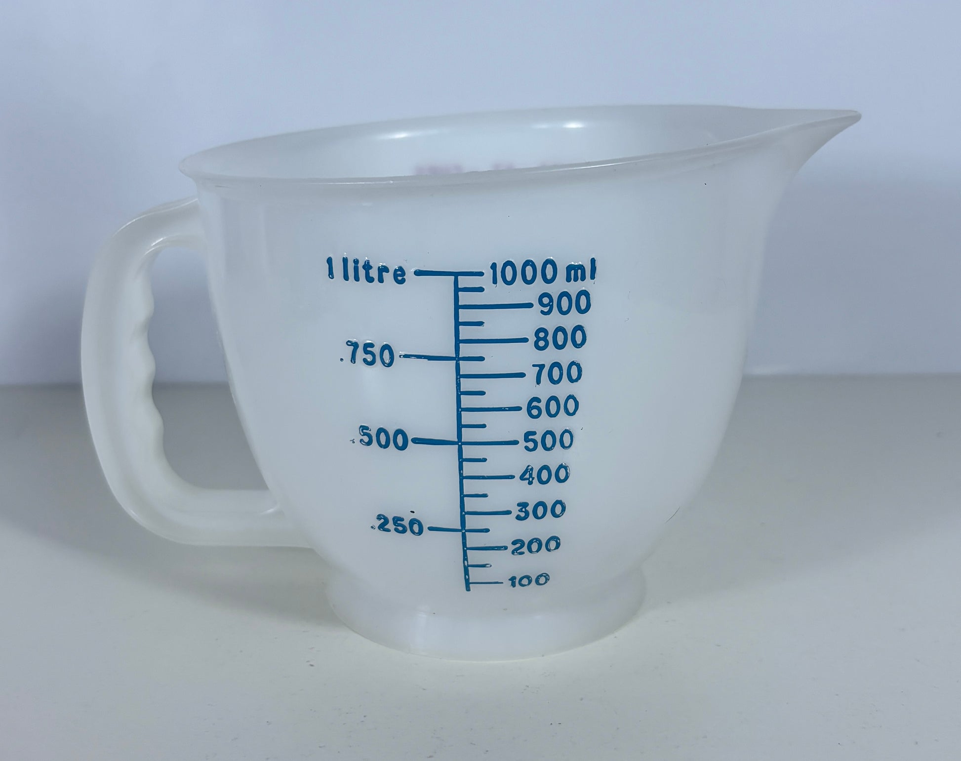 A translucent white plastic measuring jug with blue printed measurement markings in litres and millilitres, set against a plain light background.