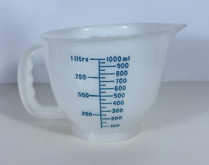 A translucent white plastic measuring jug with blue printed measurement markings in litres and millilitres, set against a plain light background.