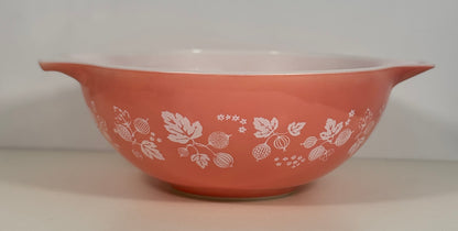A vintage Pyrex mixing bowl in a terracotta pink color with a white berry and leaf pattern, featuring a white interior and side handles.