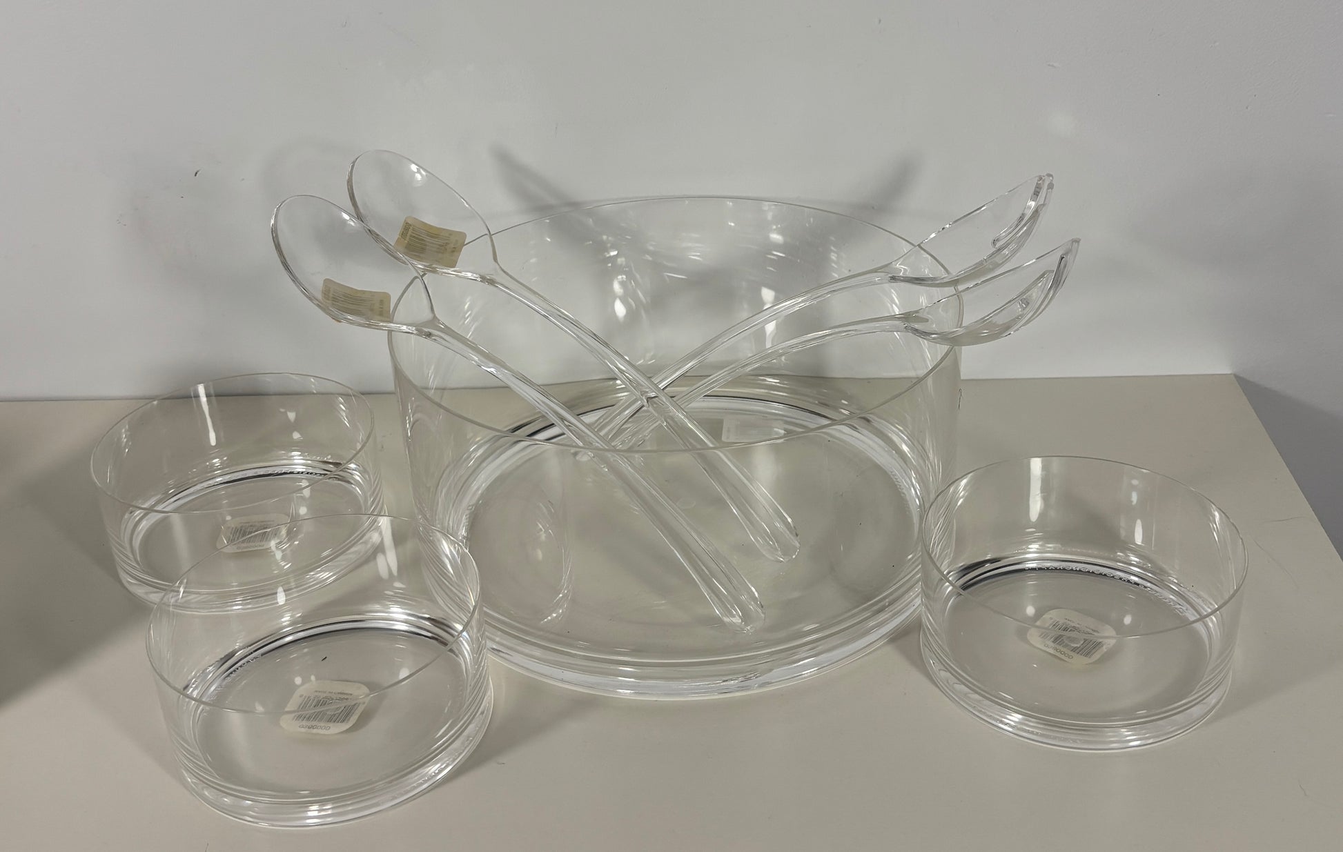 Clear glass serving pieces including a bowl, ladle, and small dishes on a light surface.