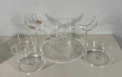 Clear glass serving pieces including a bowl, ladle, and small dishes on a light surface.