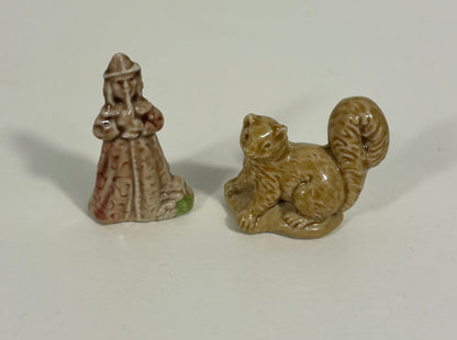 Two small ceramic figurines on a plain light background: a standing robed figure with brown and beige patterning and a small green accent at the base, and a tan squirrel figurine with a glossy finish.