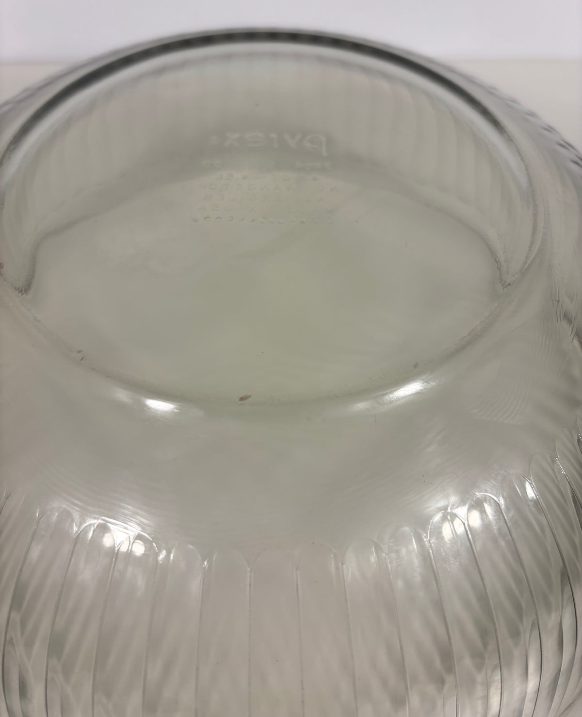 A close-up of a clear ribbed glass bowl or vase viewed from the inside, showing a faint embossed brand mark and vertical fluted texture.