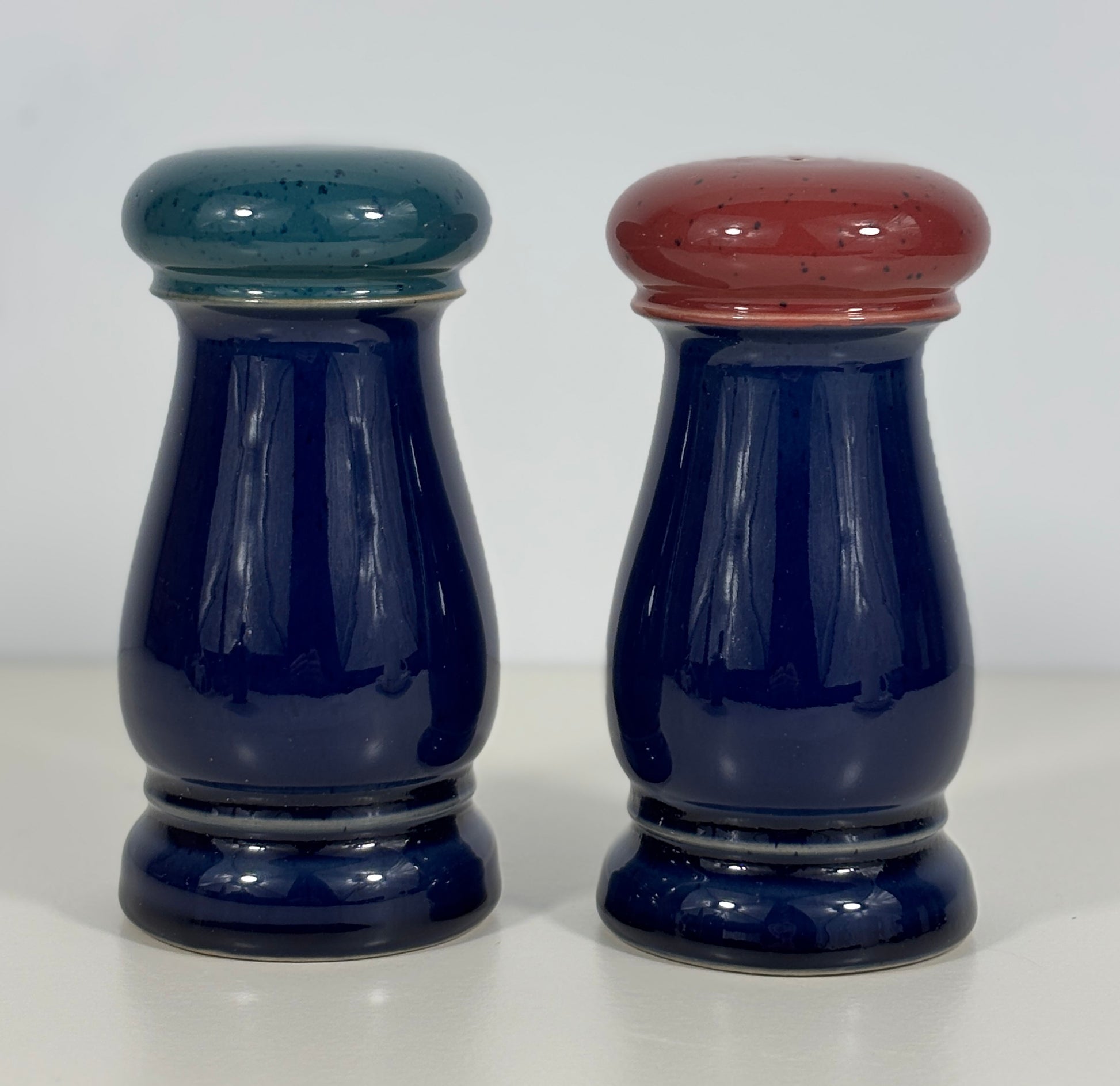 Two blue ceramic salt and pepper shakers with colored tops on a white background