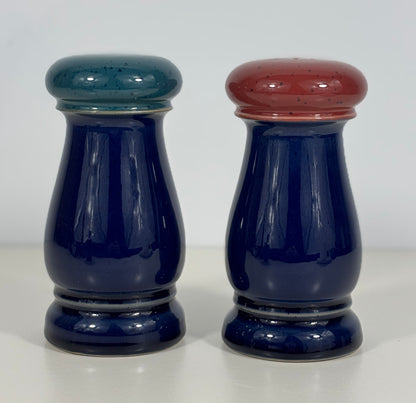 Two blue ceramic salt and pepper shakers with colored tops on a white background