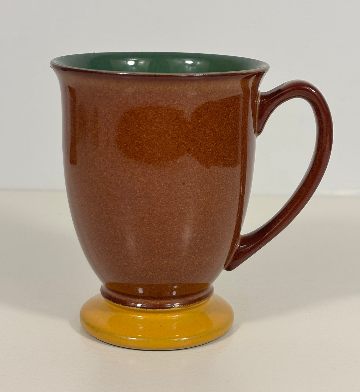 A ceramic mug with a textured brown exterior, a dark green interior, and a mustard yellow base, shown on a plain light background.