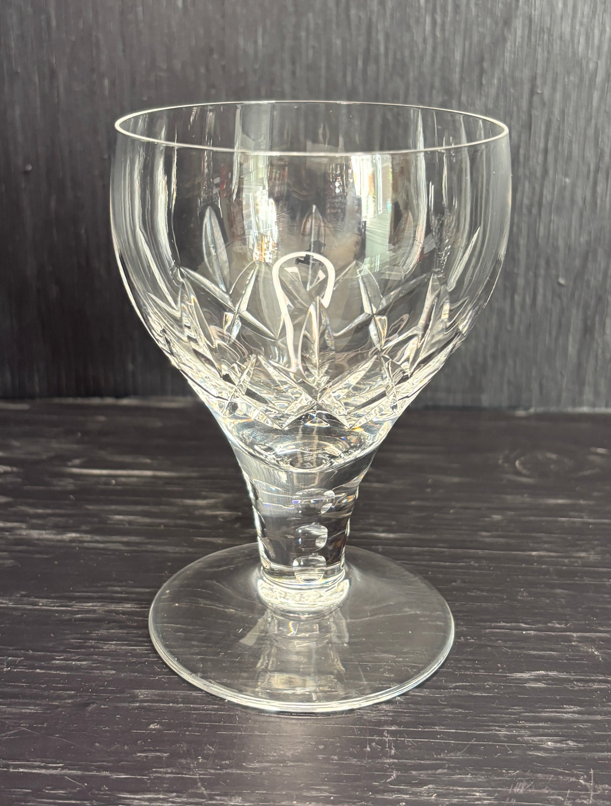 Clear glass goblet with intricate cut design on a dark wooden surface