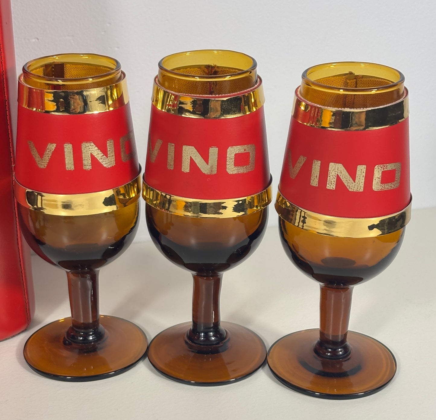 Three vintage amber glass wine glasses with red bands and gold trim, featuring the word 'VINO' in gold lettering on the red bands.