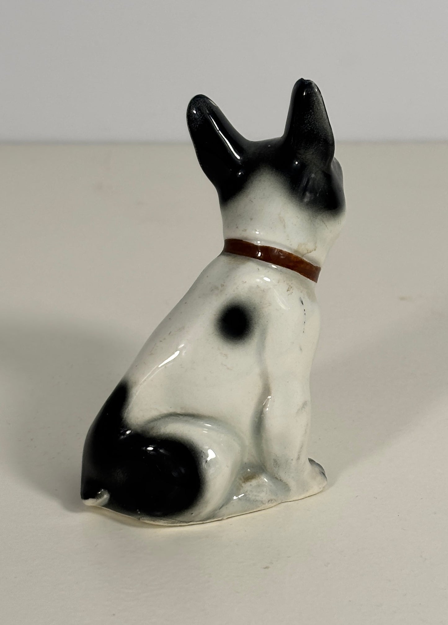 Small ceramic figurine of a black and white dog with a brown collar on a plain background