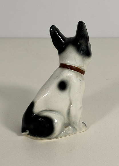 Small ceramic figurine of a black and white dog with a brown collar on a plain background