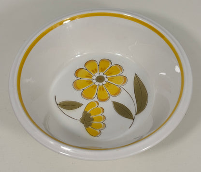A white ceramic bowl featuring a yellow floral pattern and a yellow-gold rim, photographed from a top-down angle on a light neutral background.