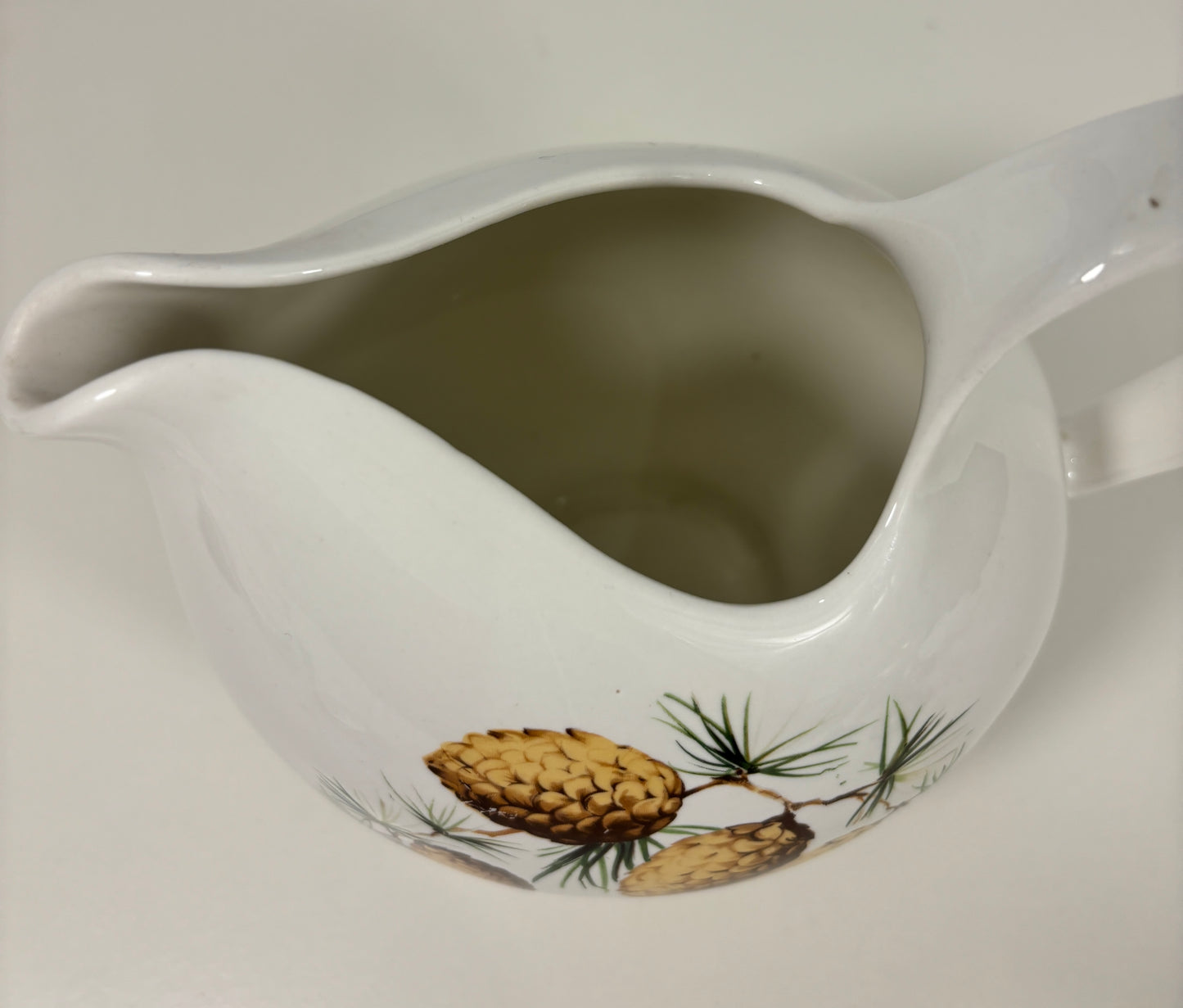 White ceramic pitcher with pine cone design on a white background