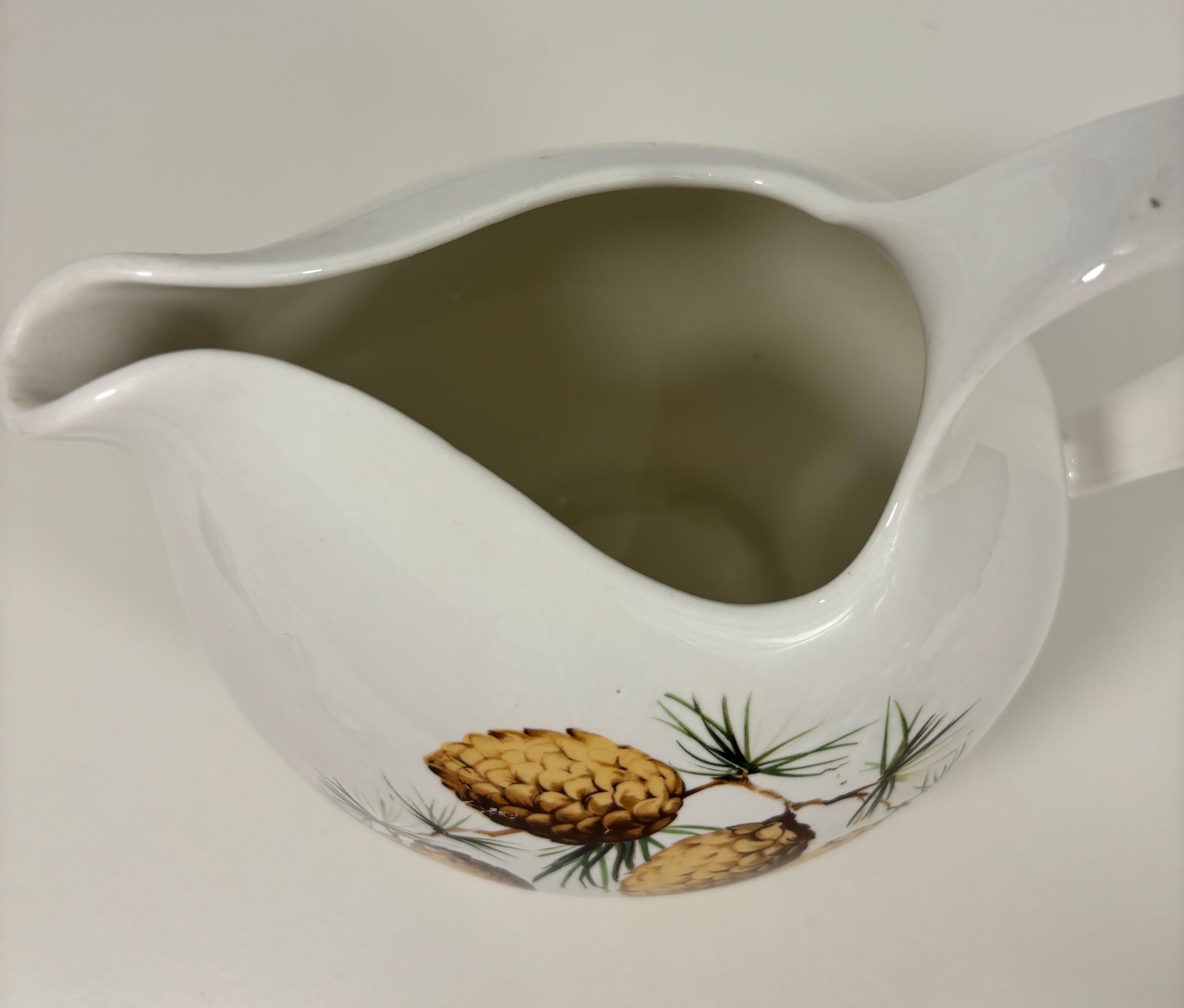 White ceramic pitcher with pine cone design on a white background
