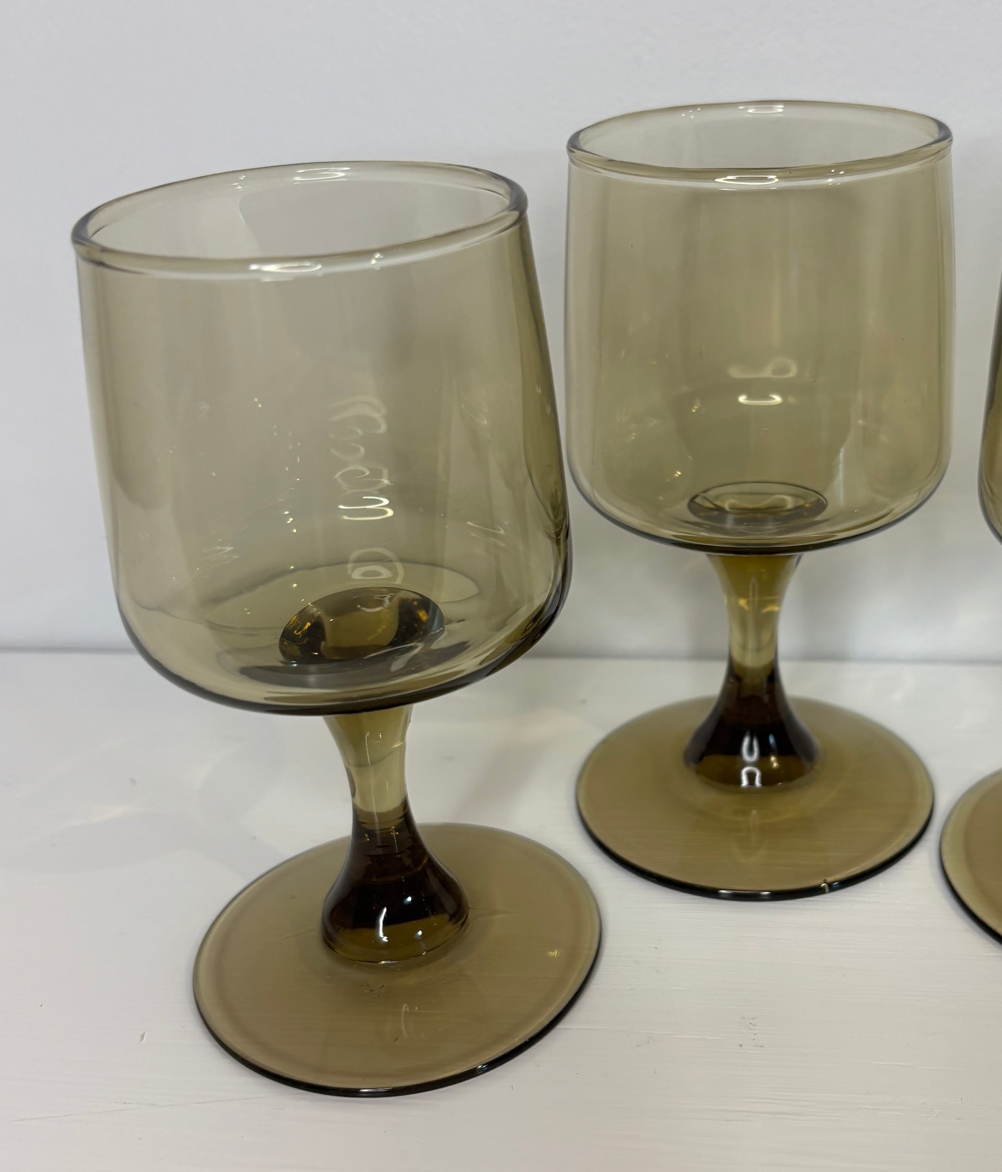 Set of three smoked glass goblets on a white surface with a white background