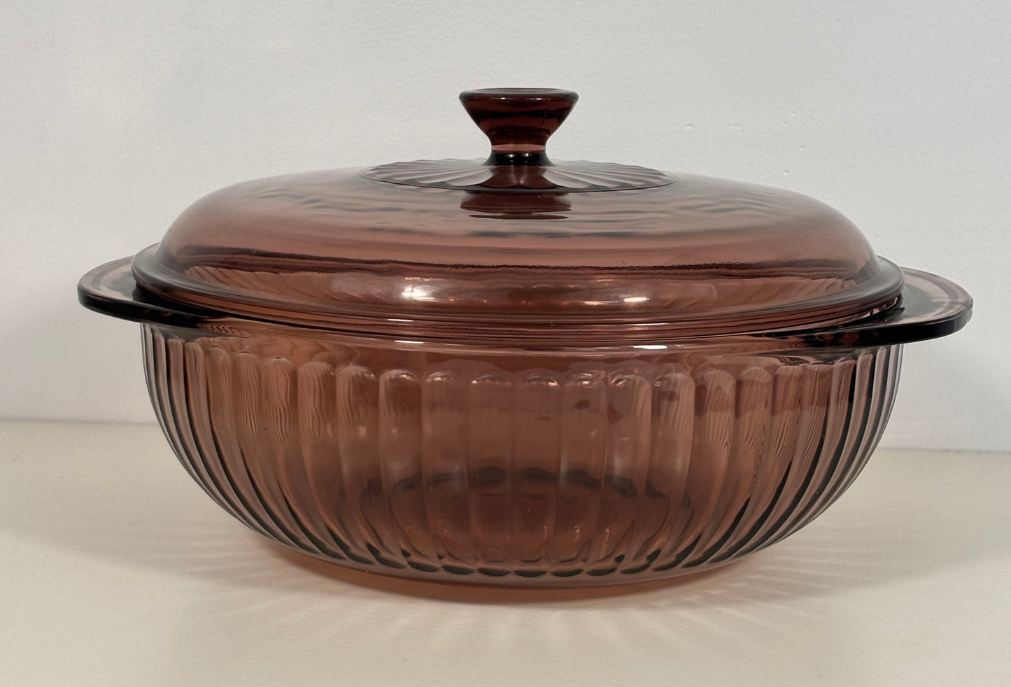 A vintage amber-brown ribbed glass casserole dish with a matching lid, shown on a plain light background.