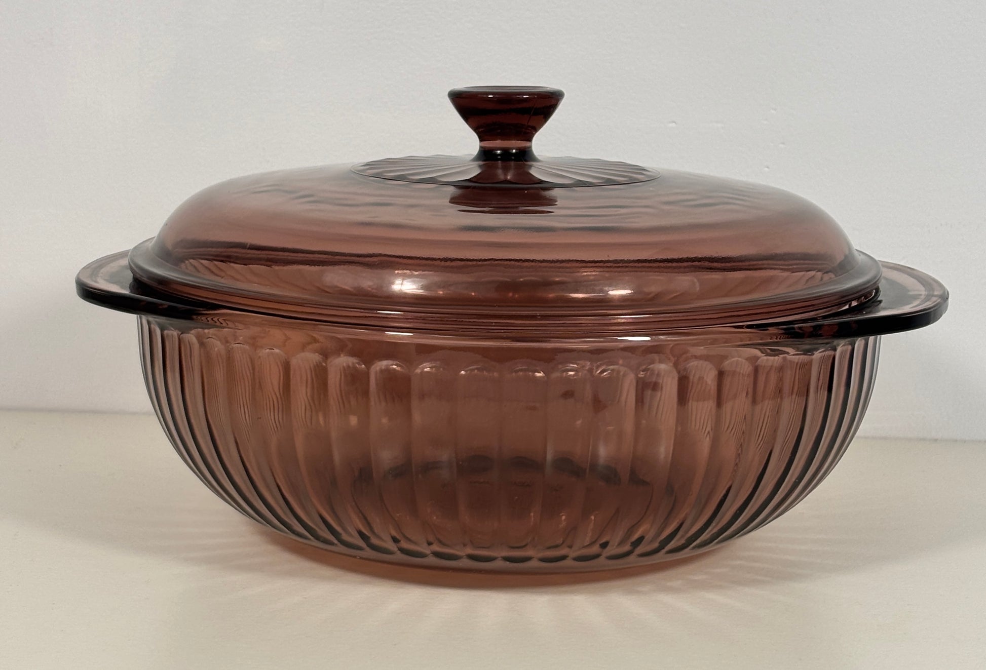 A vintage amber-brown ribbed glass casserole dish with a matching lid, shown on a plain light background.