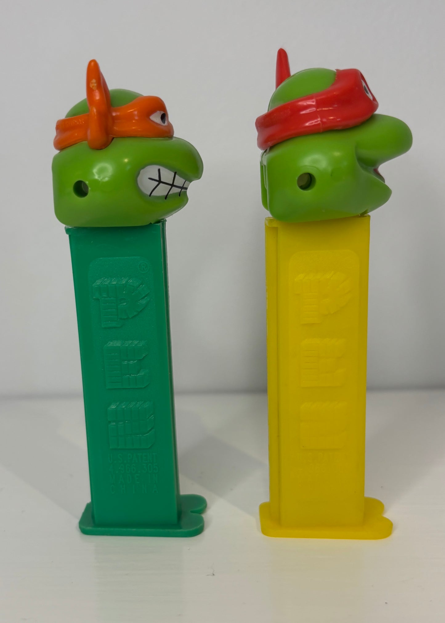 Two green turtle-shaped PEZ dispensers with red and orange headbands on a white background