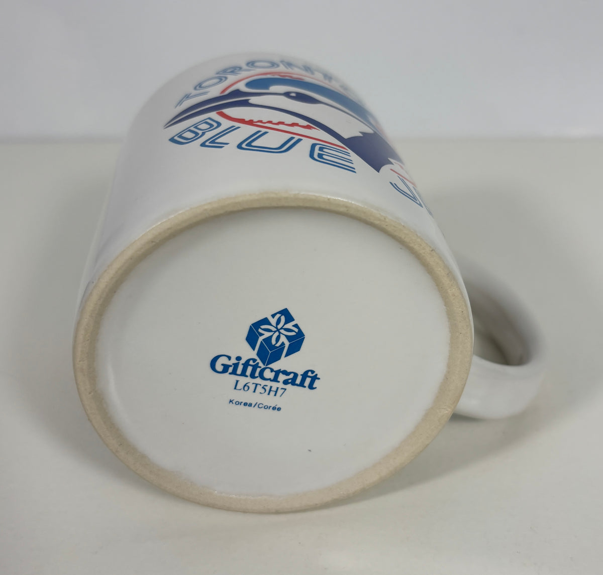 A white ceramic Toronto Blue Jays mug shown upside down, displaying the blue and red team logo on the side and the Giftcraft maker's mark on the bottom base.