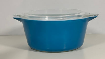 A bright blue glass casserole dish with a clear glass lid, featuring side handles, set against a plain light gray background.