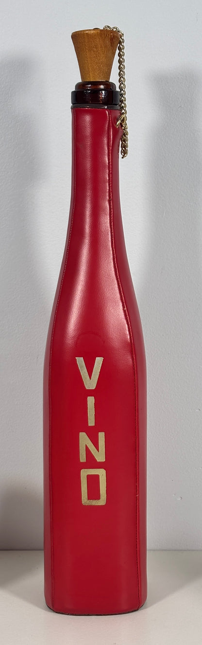 A red wine bottle-shaped decorative object with the word 'VINO' printed vertically in gold on the front, topped with a cork stopper and a small hanging chain, shown against a plain light background.