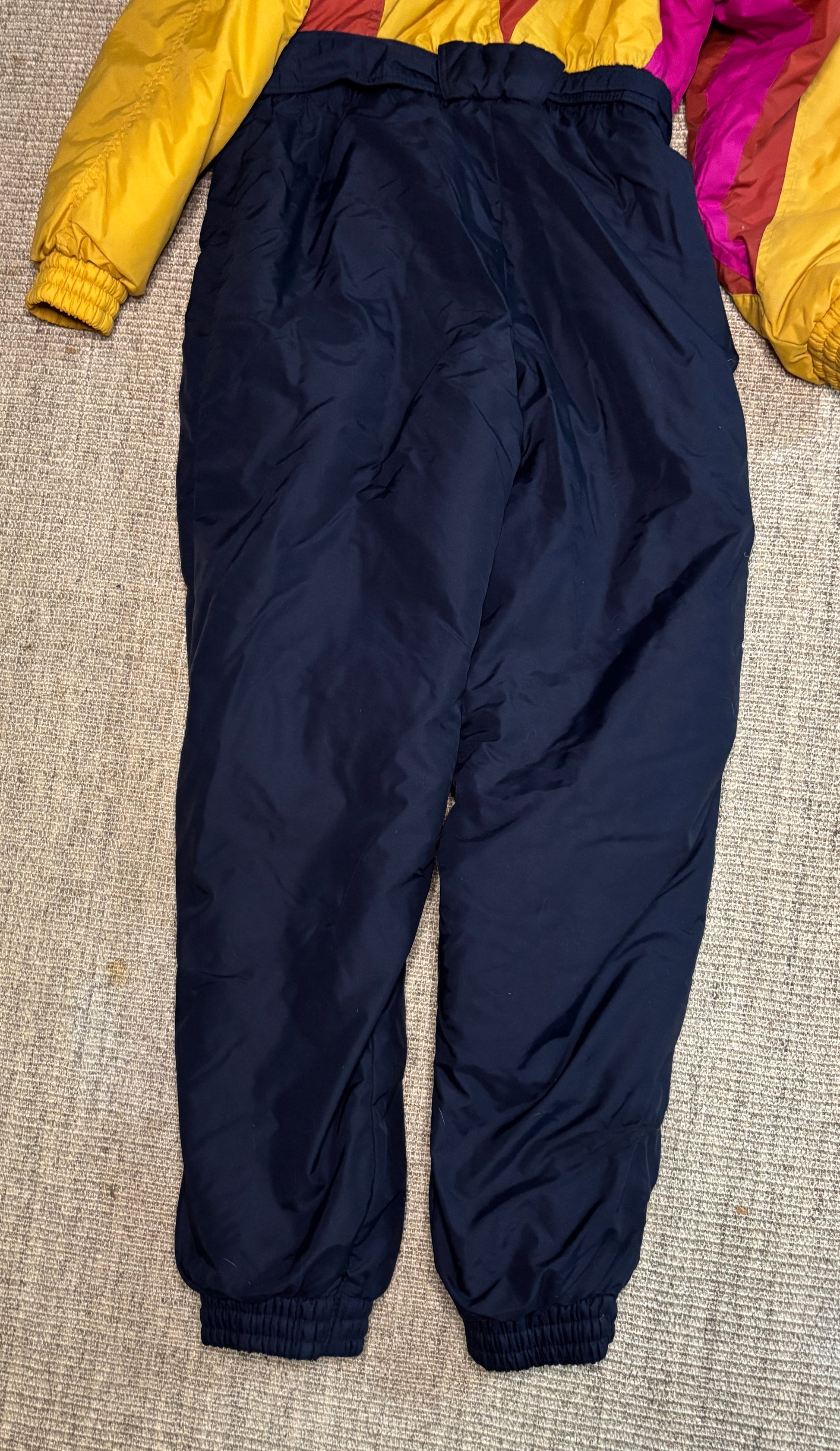 Navy blue snow pants on a textured surface with colorful fabric in the background